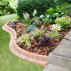 a garden with flowers and plants growing in the ground next to a brick wall on grass