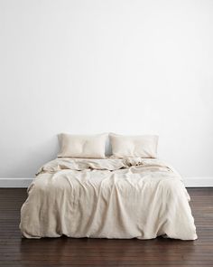 an unmade bed with two pillows on top of it in a white walled room