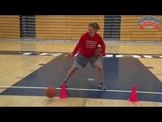 a young man holding a basketball on top of a hard wood floor next to orange cones