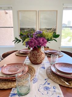 the table is set with pink and purple flowers in a vase on top of it