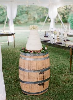 a wedding cake sitting on top of a wooden barrel in the middle of a field