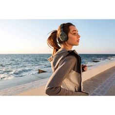 a woman with headphones on walking along the beach near the ocean in front of her