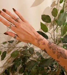 a woman's hand with tattoos and rings on her left arm next to a potted plant