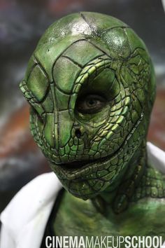 a close up of a person with green skin and an alien like face wearing a white shirt