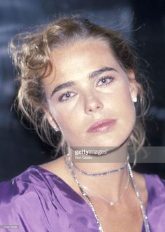 a woman wearing a purple dress and pearls in her hair, looking at the camera