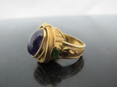 "Incredible SeidenGang Athena Collection heavy weight 18k yellow gold ring. Large oval cabochon Amethyst centerpiece or flip for engraved Athena, flanked by 2 green Tourmalines. Amethyst measures 13.4 mm x 9mm. Each Tourmaline measures 3.2 mm x 2.2mm. Top to bottom measures 7/8\" x 5/8\" side to side. Ring size 7.5. Hallmarks at inner ring. Total weight of 18.7 grams. 10464-2" Luxury Formal Cabochon Amethyst Ring, Luxury Formal Amethyst Cabochon Ring, Luxury Amethyst Cabochon Ring For Formal Occasions, Formal Cabochon Amethyst Ring Fine Jewelry, Formal Yellow Gold Cabochons With Bezel Setting, Yellow Gold Multi-stone Cabochons For Gift, Luxury Yellow Gold Amethyst Ring Oval Cabochon, Formal Yellow Gold Cabochon Sapphire Ring, Gold Domed Gemstone Cabochons