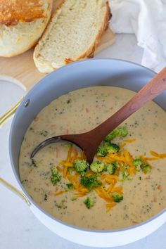 broccoli cheese soup in a blue bowl with a wooden spoon and bread on the side