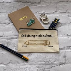 a notebook, pen and pencils sitting on top of a white brick wall