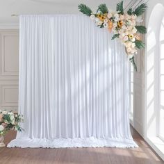 a white backdrop with flowers and greenery on the side is in front of a window