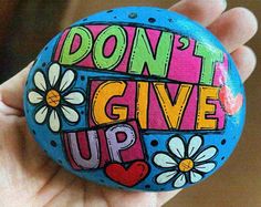 a painted rock with the words don't give up on it and daisies