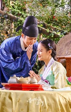 a man and woman sitting at a table in front of each other with dishes on it