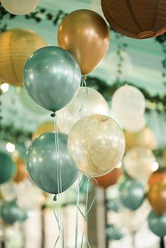 a bunch of balloons are hanging from the ceiling in a room with green and gold decorations