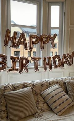 balloons that spell out happy birthday are on a window sill in front of a couch