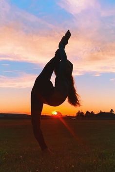 a woman doing a handstand in front of the sun with her legs up