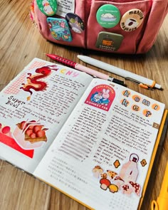 an open book on a wooden table next to some pens and pencils in a bag