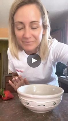 a woman sitting at a table with a bowl in front of her and strawberries on the counter