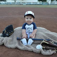 a little boy sitting on top of a baseball field next to a glove and ball