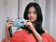 a woman in an orange dress is holding up a fake toothbrush with the image of herself on it