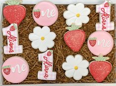 some decorated cookies in a box with strawberries and daisies on them, one is 1st birthday