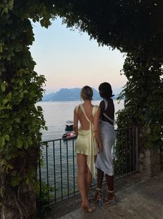 two women standing next to each other looking at the water