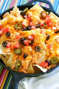 a skillet filled with nachos, cheese and black olives on a colorful table cloth