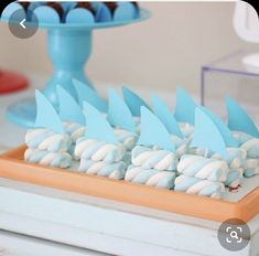 there are many blue and white desserts on the table with cupcakes in the shape of shark fin