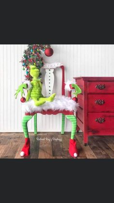 an elf sitting on top of a chair in front of a christmas tree and red dresser