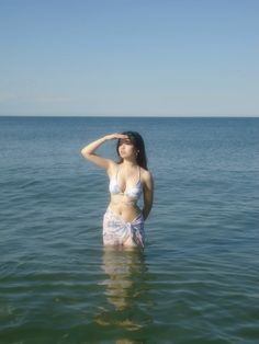 a woman is standing in the water with her hands on her head and looking off into the distance