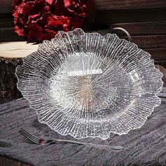 a clear glass plate sitting on top of a wooden table next to a red flower