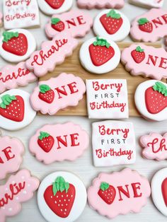 decorated cookies with names and strawberries are displayed on a wooden board for the first birthday