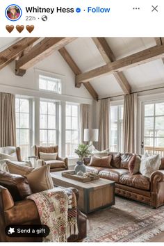 a living room filled with lots of furniture next to two large windows and wooden beams