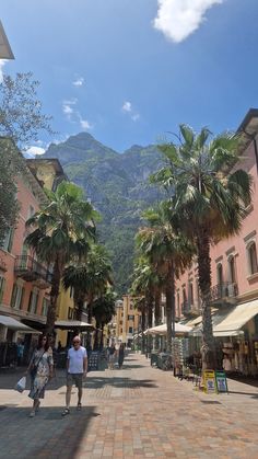 two people walking down a street with palm trees in the foreground and mountains in the background