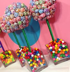 three vases filled with candy sitting on top of a pink wall next to each other