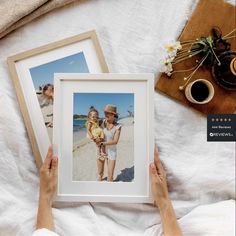 a person holding up two pictures in front of them on a bed with white sheets