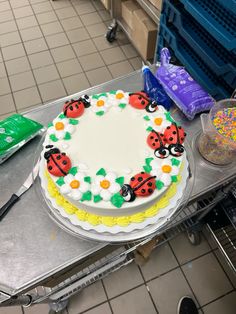 a cake with ladybugs on it sitting on top of a metal table in a kitchen