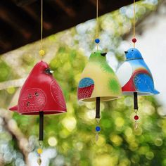 three colorful bird shaped wind chimes hanging from the ceiling in front of some trees