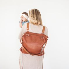 a woman carrying a baby in a brown leather backpack with her back to the camera