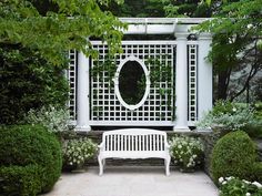 a white bench sitting in front of a pergolated wall with a mirror on it