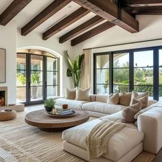 a living room with white couches and wooden beams on the ceiling, large windows