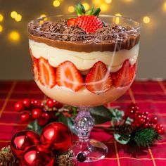 a dessert dish with strawberries and chocolate in it on a red tablecloth next to christmas decorations