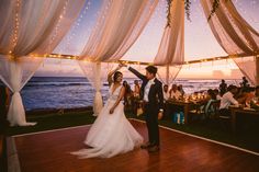 a bride and groom dancing on the dance floor in front of an ocean at sunset