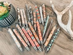 many pens are lined up on a table next to a deer antler and flower pot