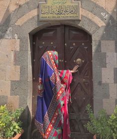 a woman standing in front of a door wearing a colorful shawl over her head