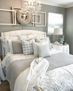 a white bed sitting under a chandelier next to a window in a bedroom