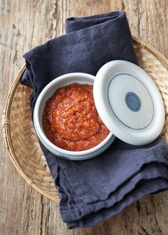 a white bowl filled with red sauce on top of a blue cloth next to a wooden table