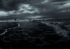 black and white photograph of waves crashing on the beach with dark clouds in the background