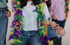 a woman in a white shirt and purple and green feathers around her neck, standing next to two other people