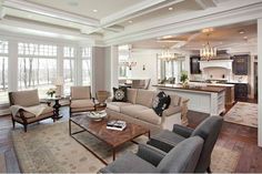 a living room filled with furniture next to a kitchen and breakfast nook in front of large windows