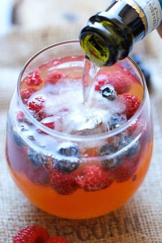 a person pouring wine into a glass filled with berries