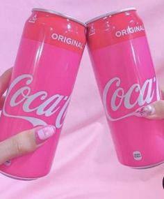 two pink coca - cola cans are being held up